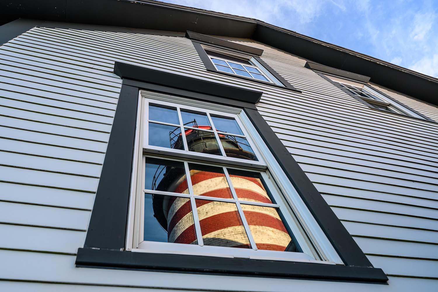 A picture of a lighthouse reflected in the window of a home